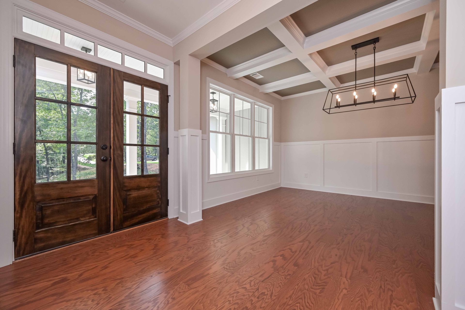 Empty dining room with wood floors, doors, and white paneled walls.