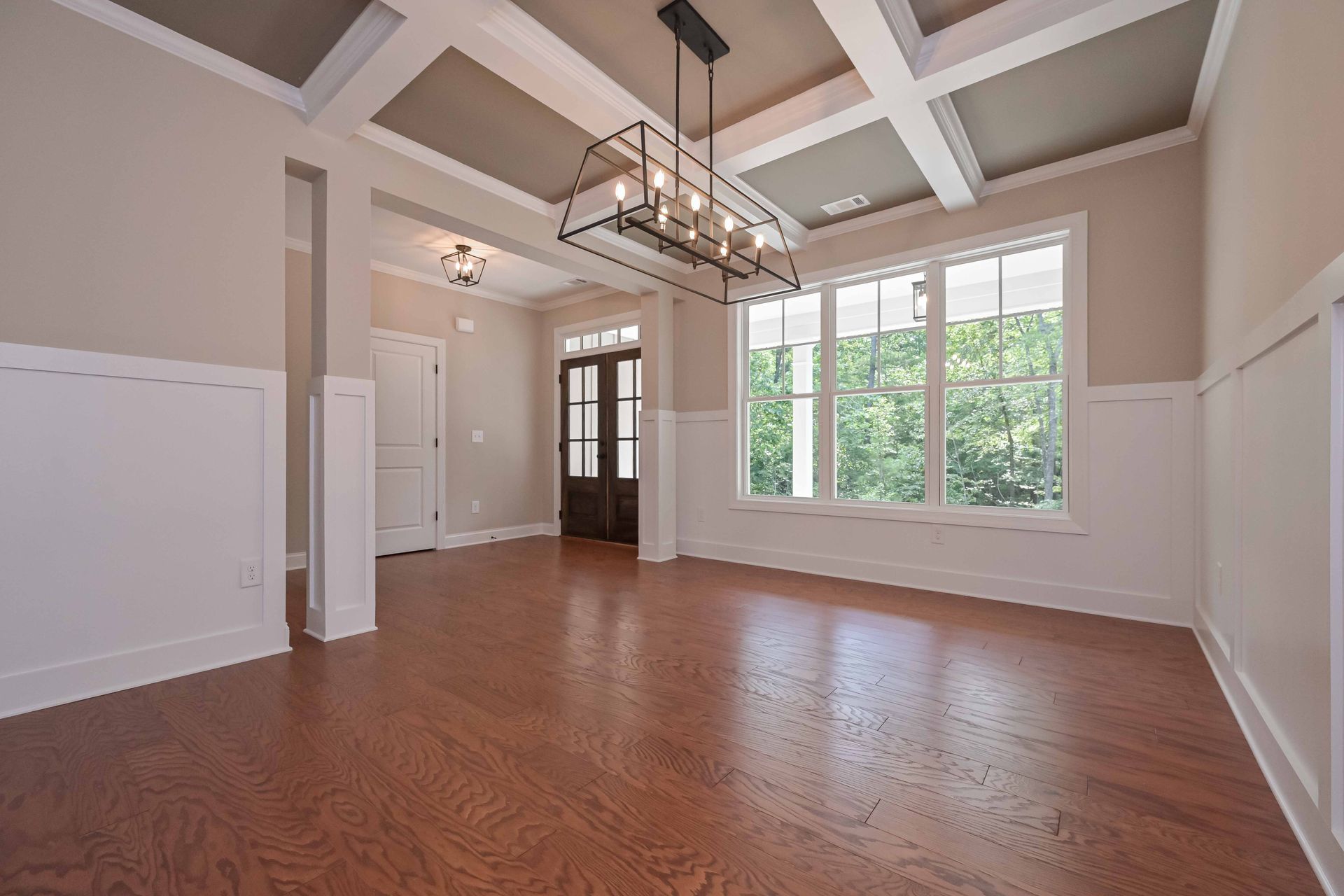 Empty dining room with hardwood floor, neutral walls, white trim, and a coffered ceiling.