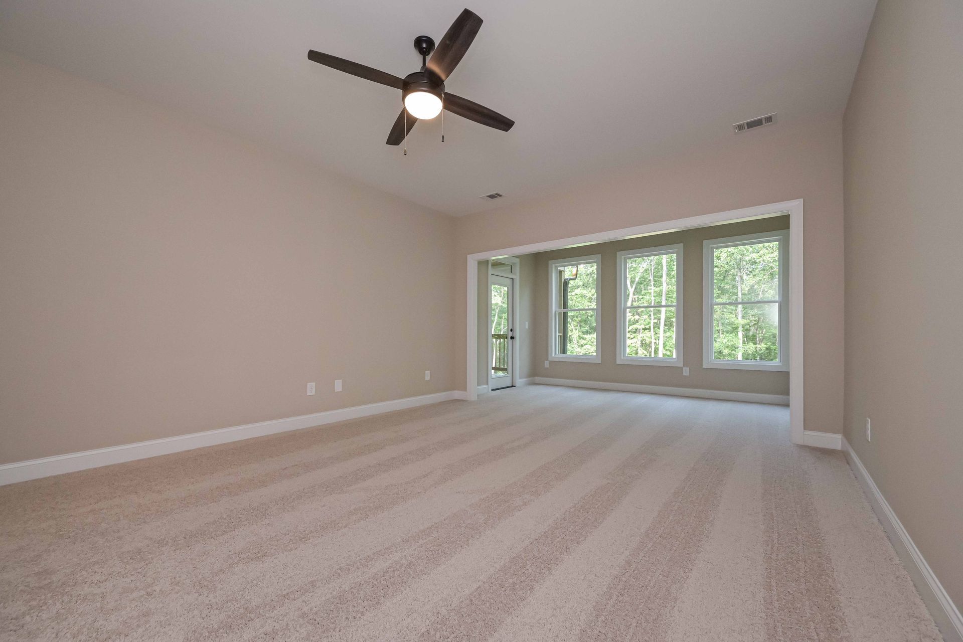 Empty room with beige walls, light carpet, ceiling fan, and large windows.