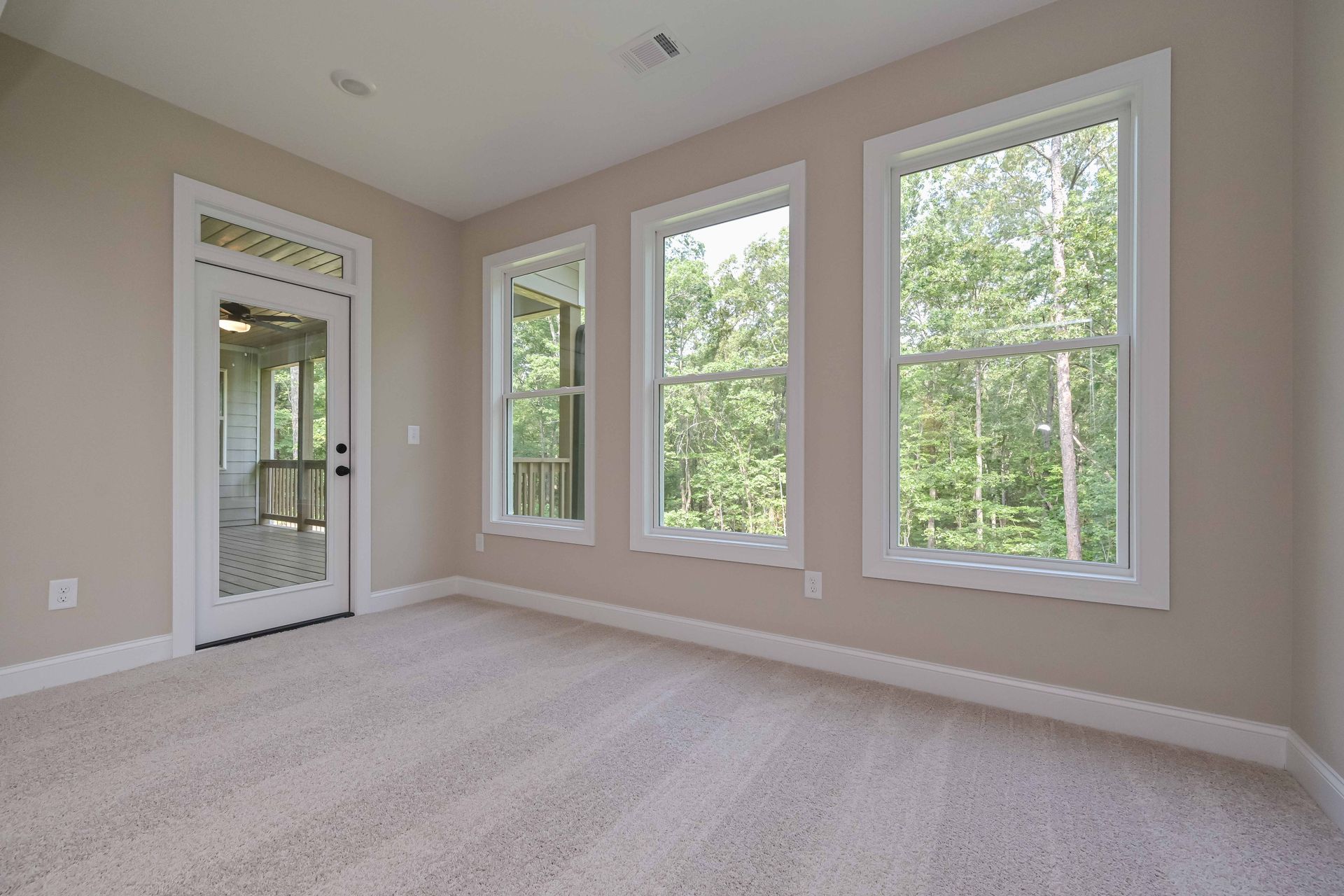 Empty room with three windows and door, beige carpet, neutral walls, natural light.
