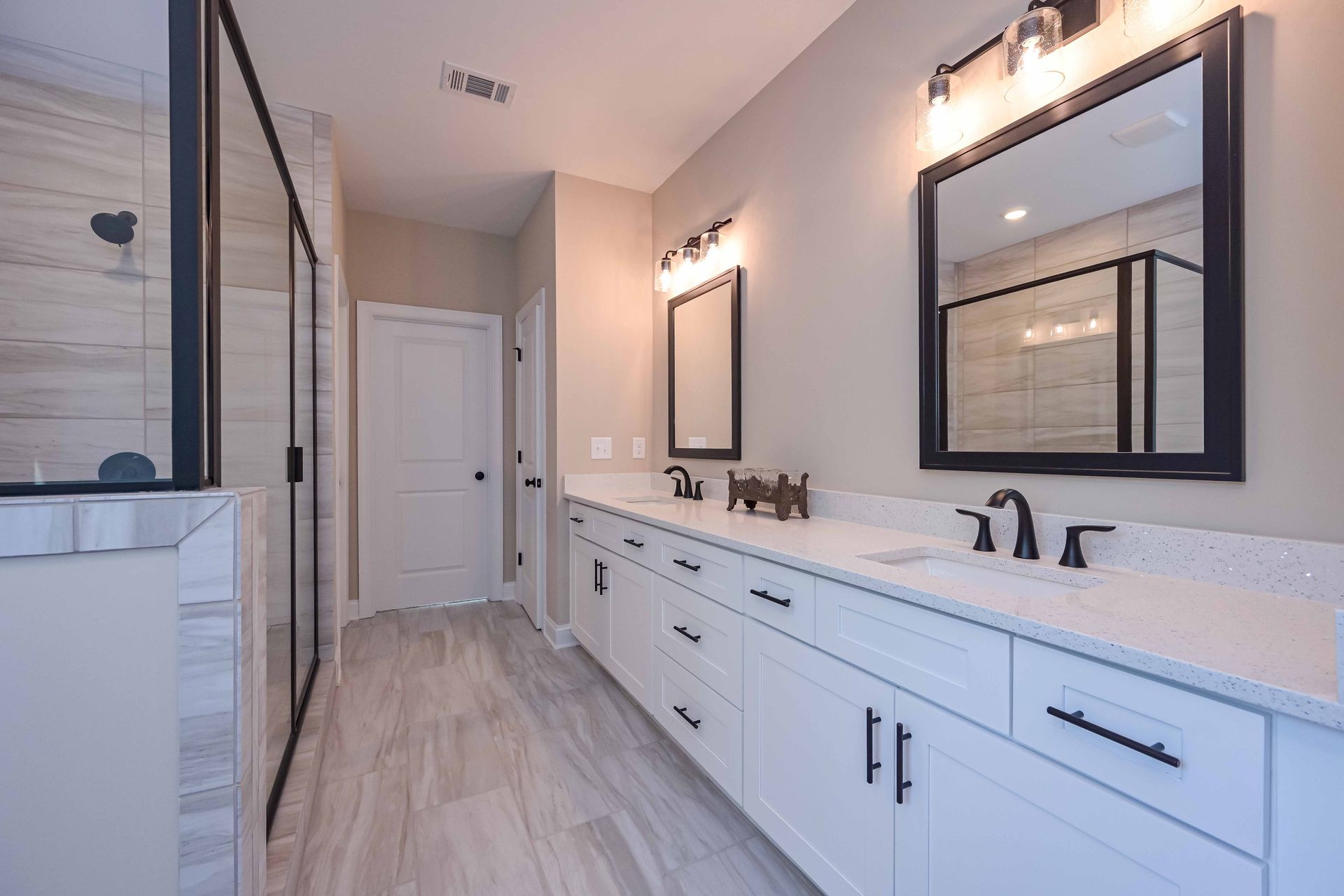 Modern bathroom with double vanity, walk-in shower, and white cabinets.