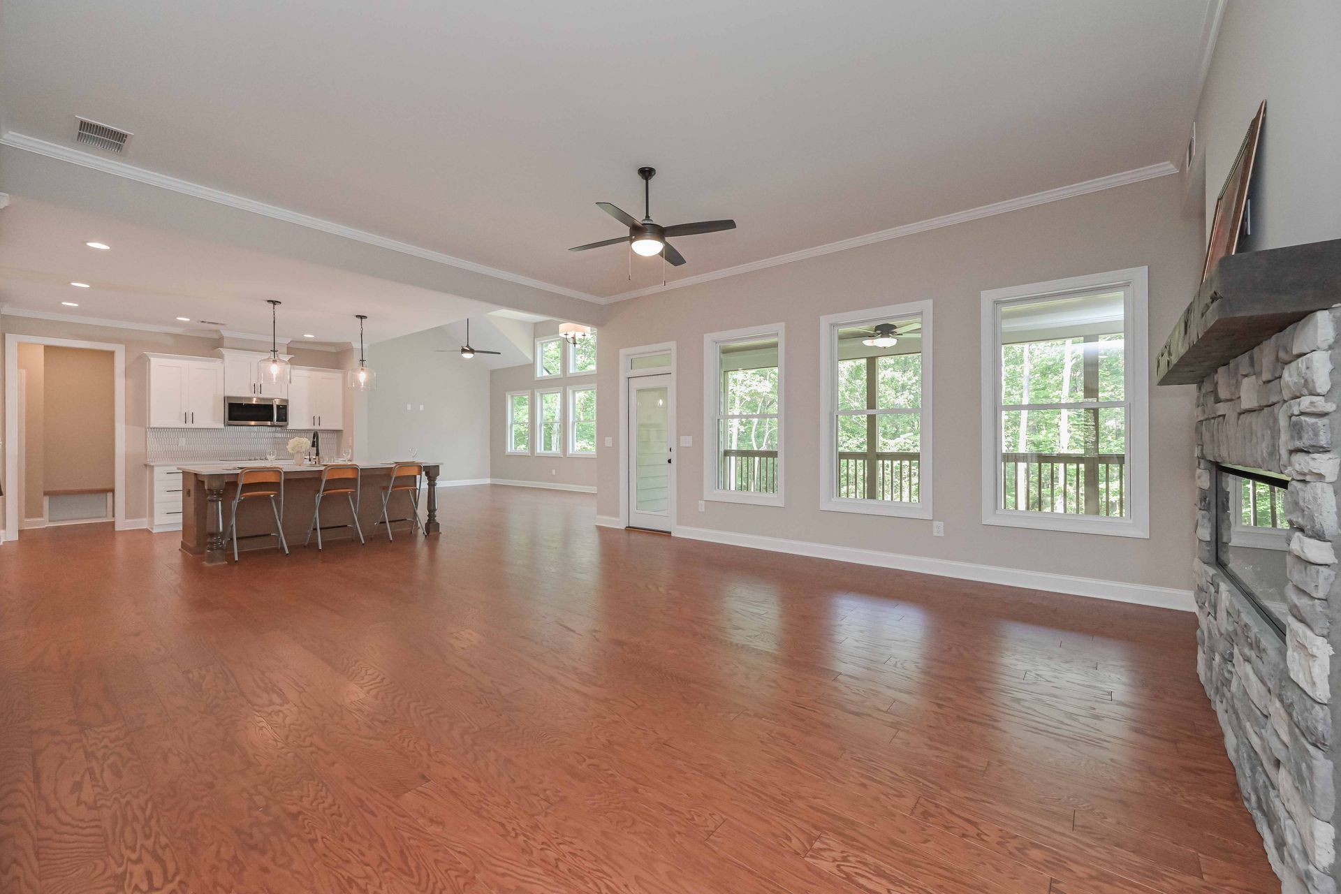 Spacious living area with wood floors, open kitchen, fireplace, and large windows with natural light.