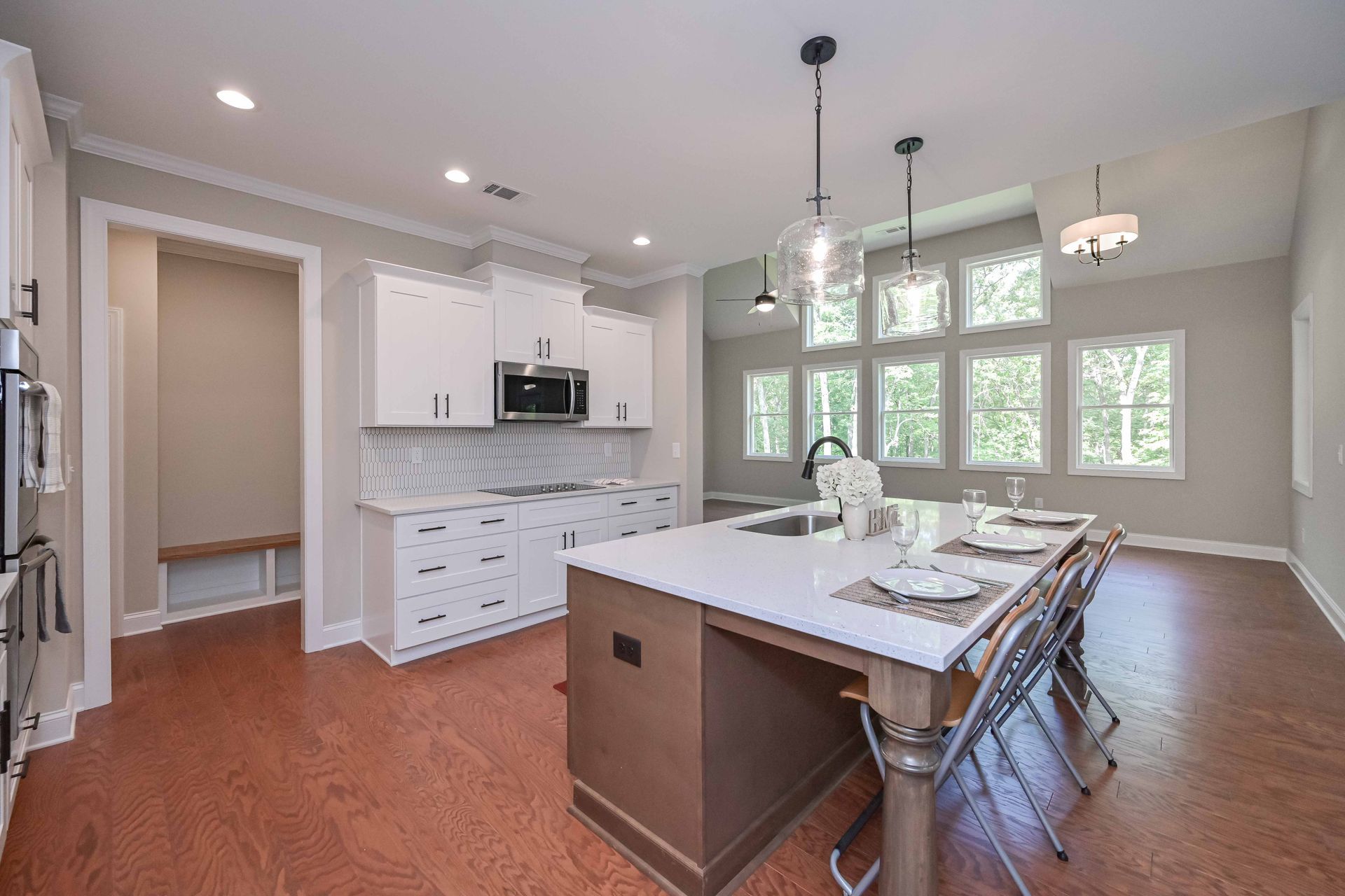 Modern kitchen with white cabinets, island with seating, large windows, and wood flooring.