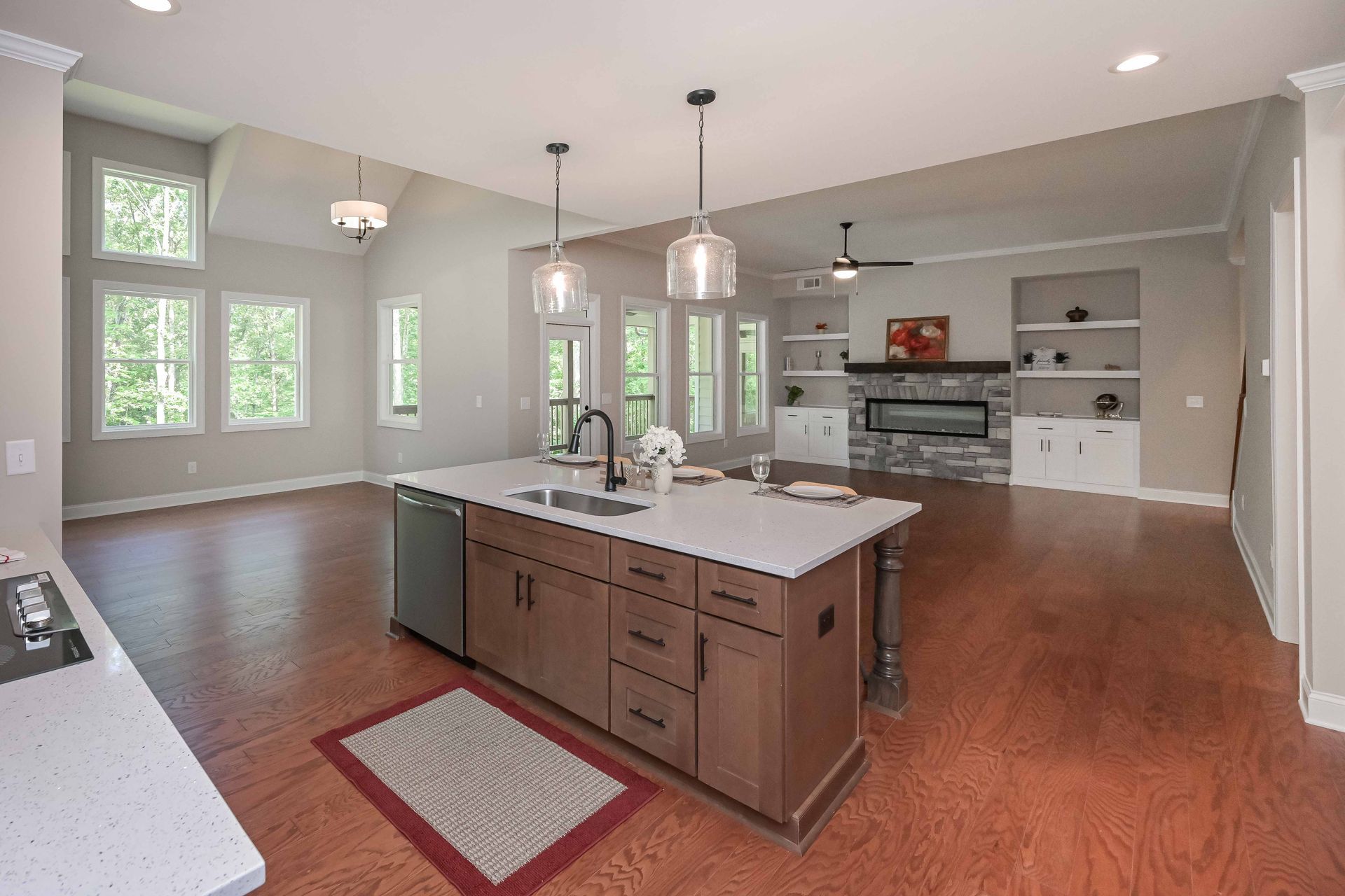 Open-concept kitchen with island, sink, and cabinetry. Living area with fireplace, built-ins, and windows; wood floors.