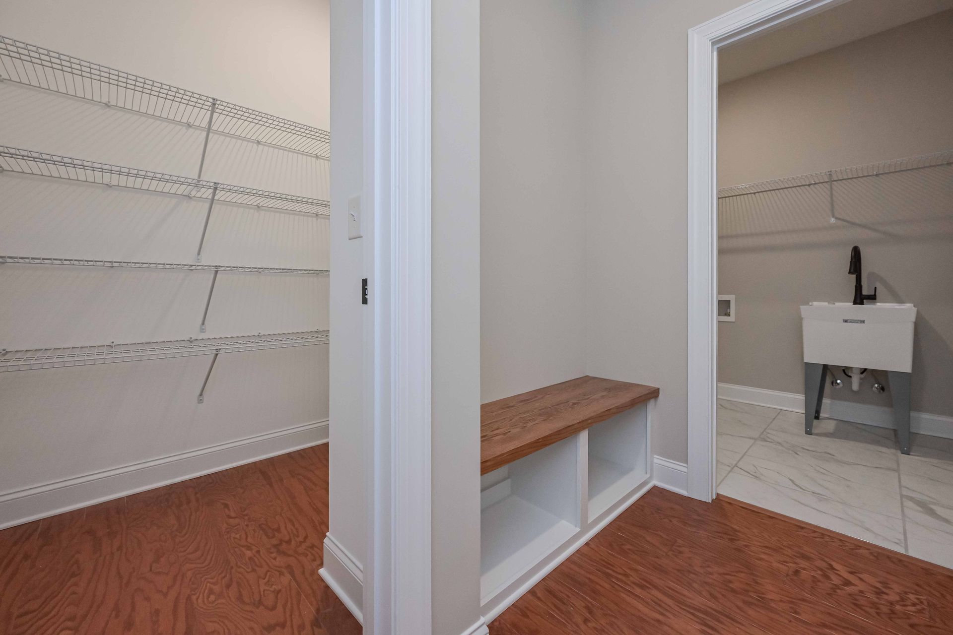 Hallway with shelving, bench, and laundry room entrance; wood floors, white walls.