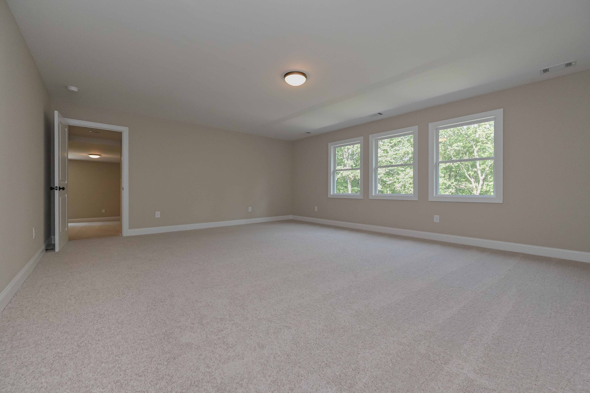 Empty, carpeted room with neutral walls, three windows, and a doorway.