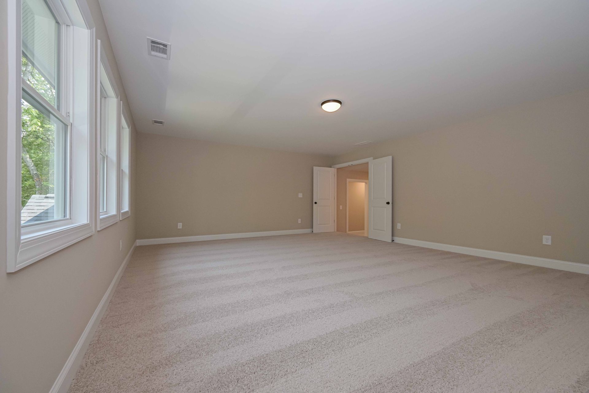 Empty beige-walled room with beige patterned carpet, white-framed windows, and a doorway.