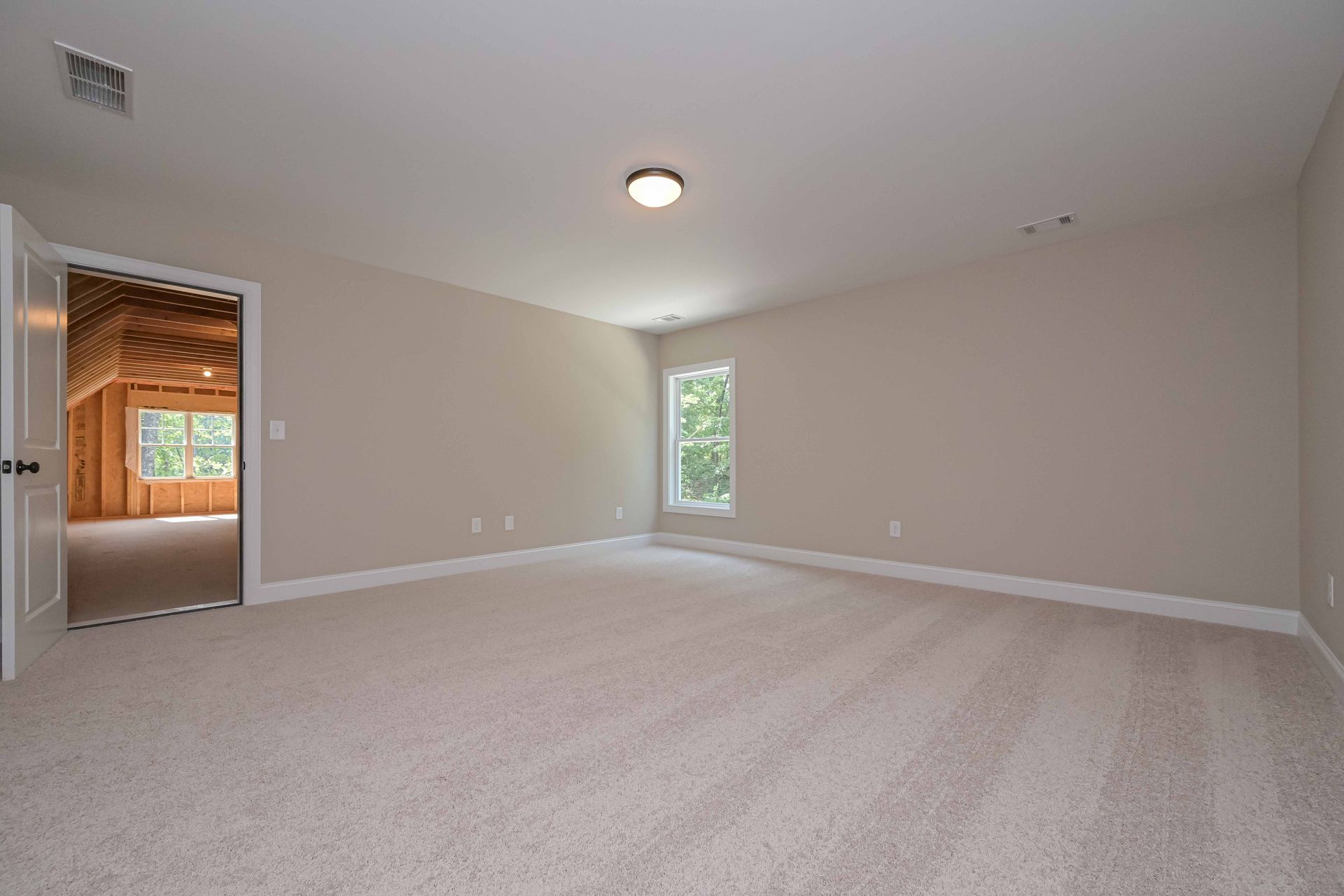 Empty beige bedroom with a doorway leading to a construction area, and a window.