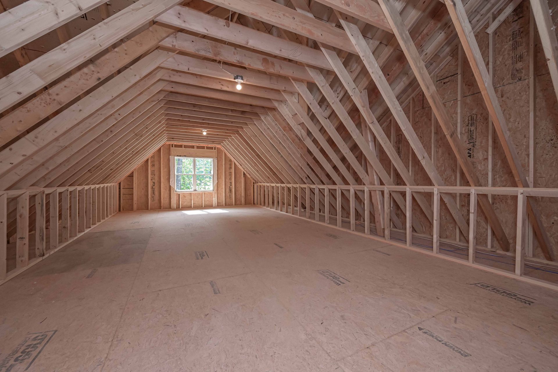 Unfinished attic space with exposed wooden beams, a small window, and light fixture.