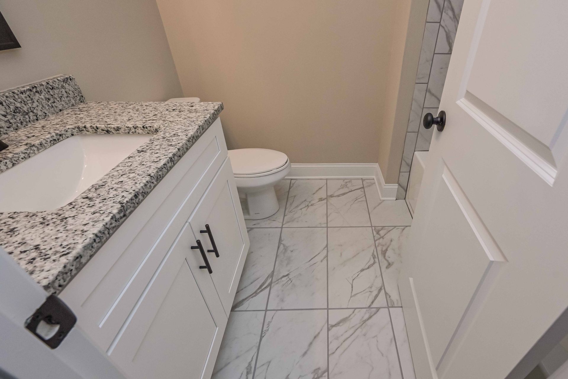 Bathroom with white vanity, marble countertop, toilet, and marble-look tile flooring.