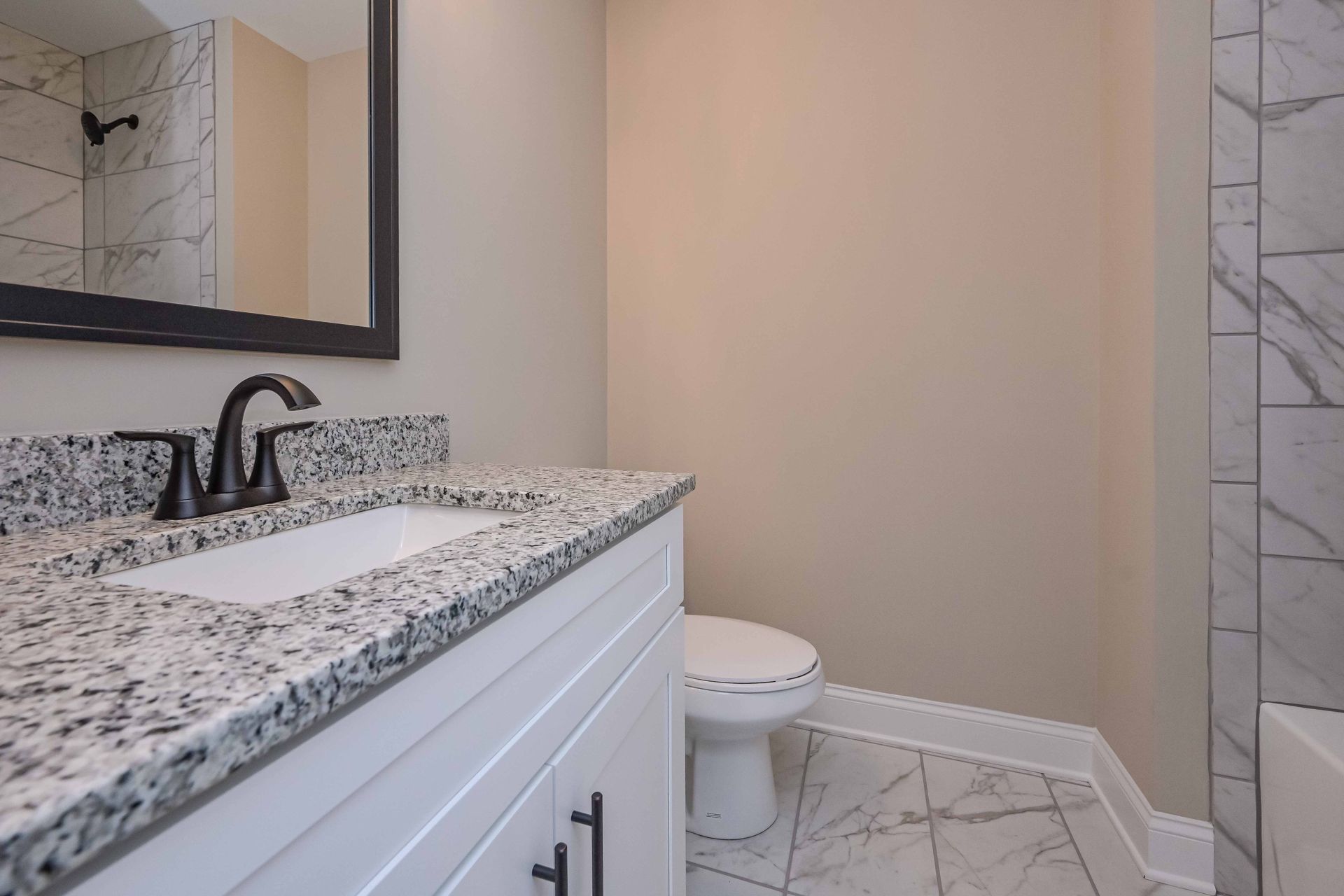 Bathroom with white cabinets, marble countertop and floor, black faucet and mirror.
