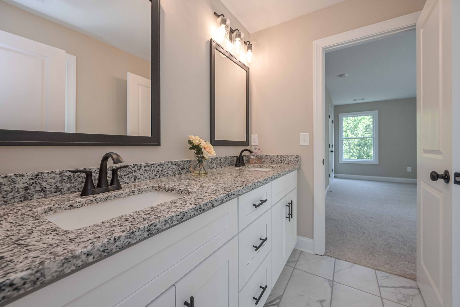 Bathroom with white cabinets, granite countertop, black fixtures, mirrors, and an open doorway.