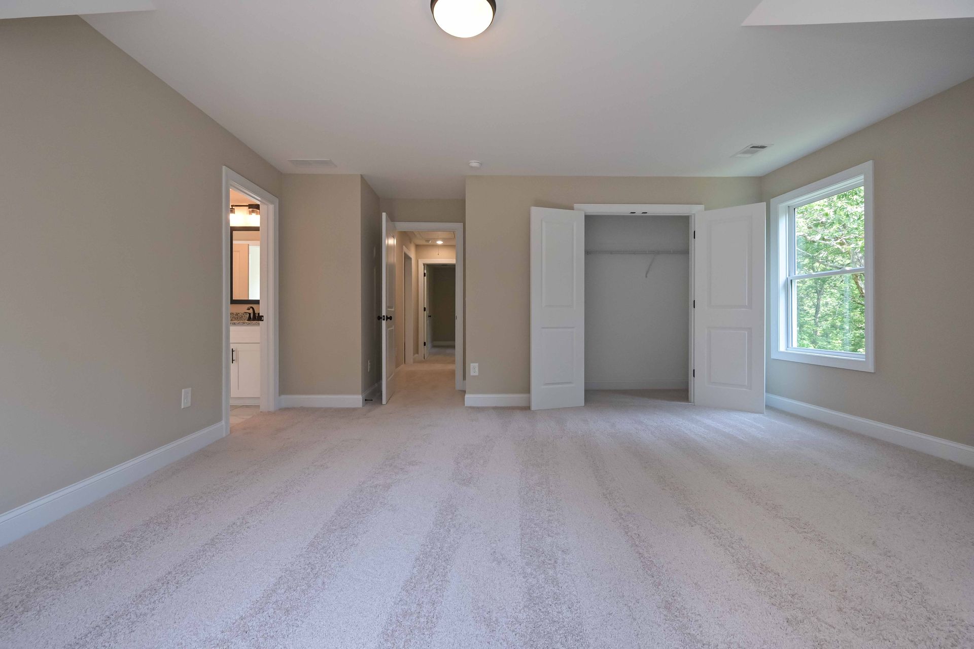 Empty beige bedroom with carpet, closet, and a window.