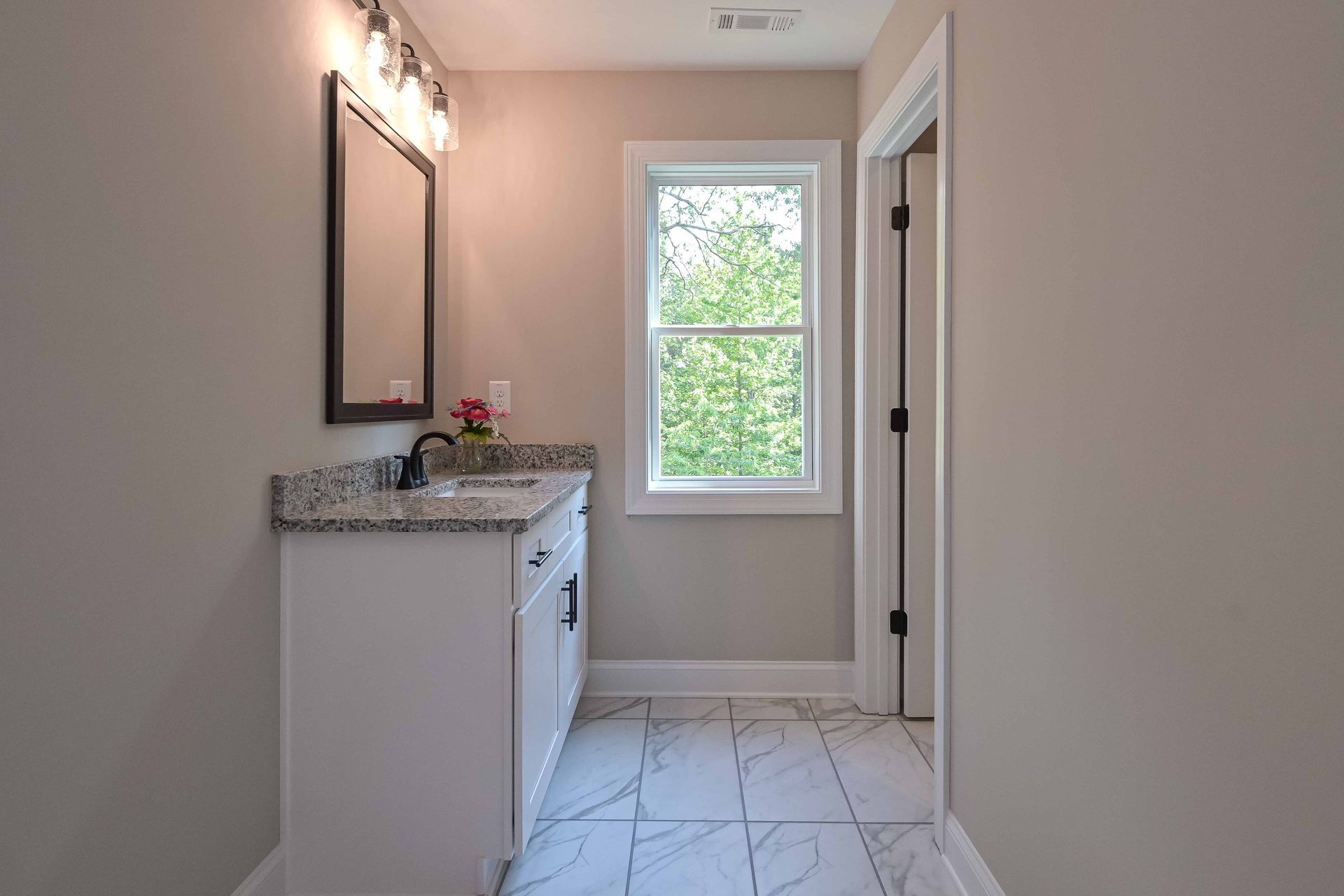 Bathroom with white vanity, gray countertop, black framed mirror, and window.