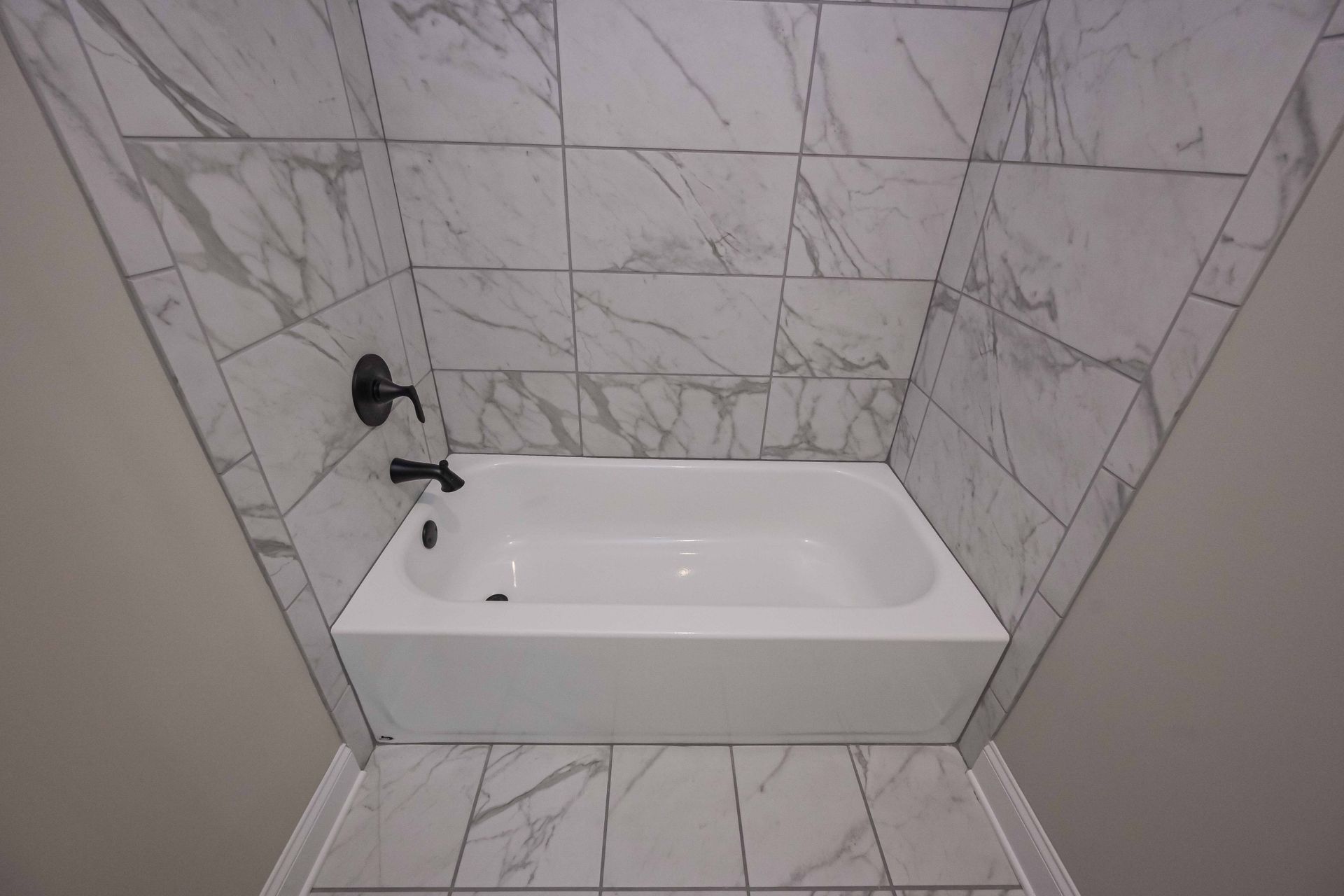 White bathtub with black faucet, surrounded by marble tile walls and floor.