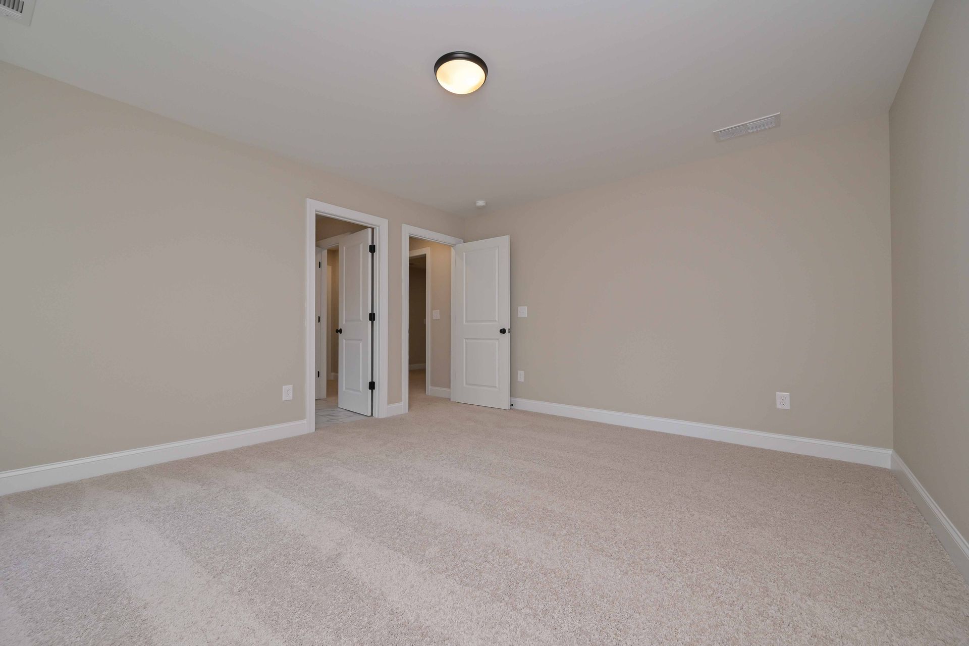 Empty room with beige walls, light-colored carpet, and two doorways. Ceiling light is centered.