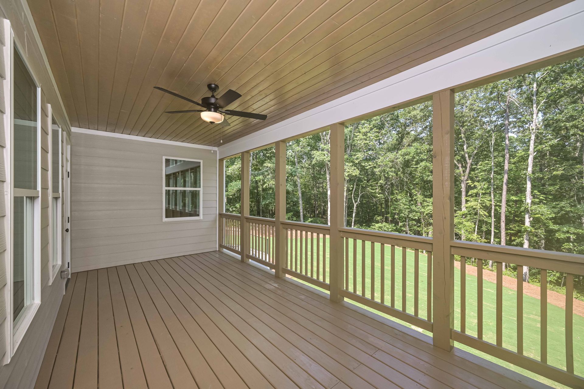 Screened porch with light brown wood floor, railing, and ceiling, with views of green trees and grass.