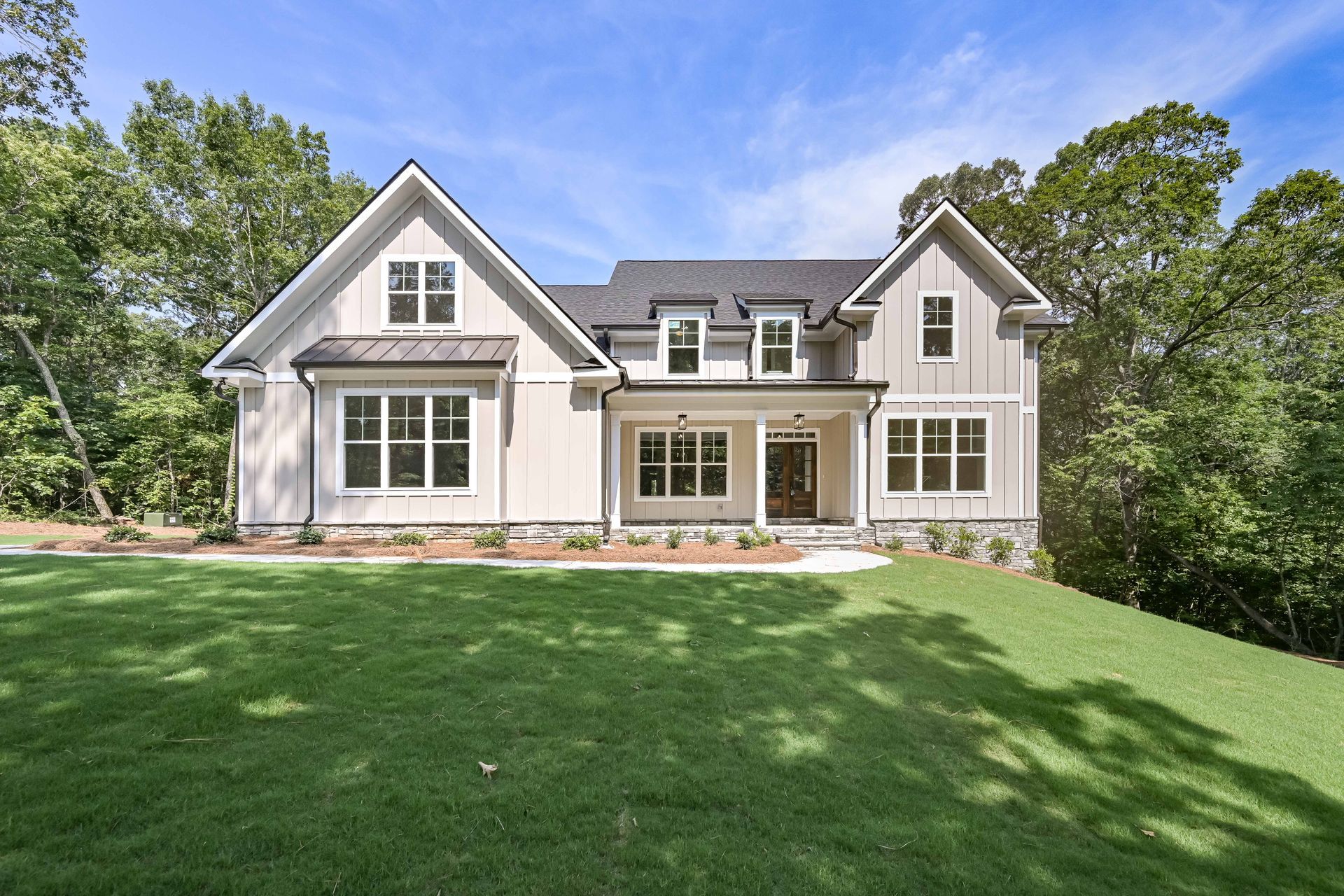 Beige two-story house with white trim, a dark roof, and a green lawn on a sunny day.