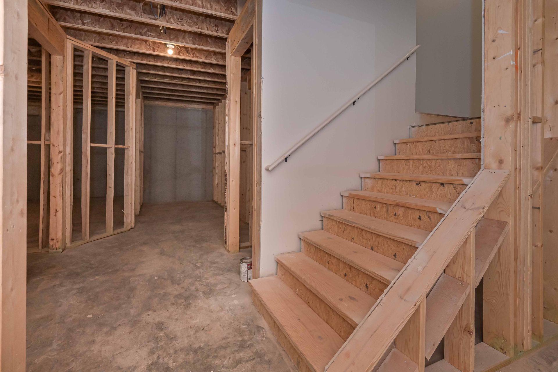 Unfinished basement with wooden stairwell and exposed framing.