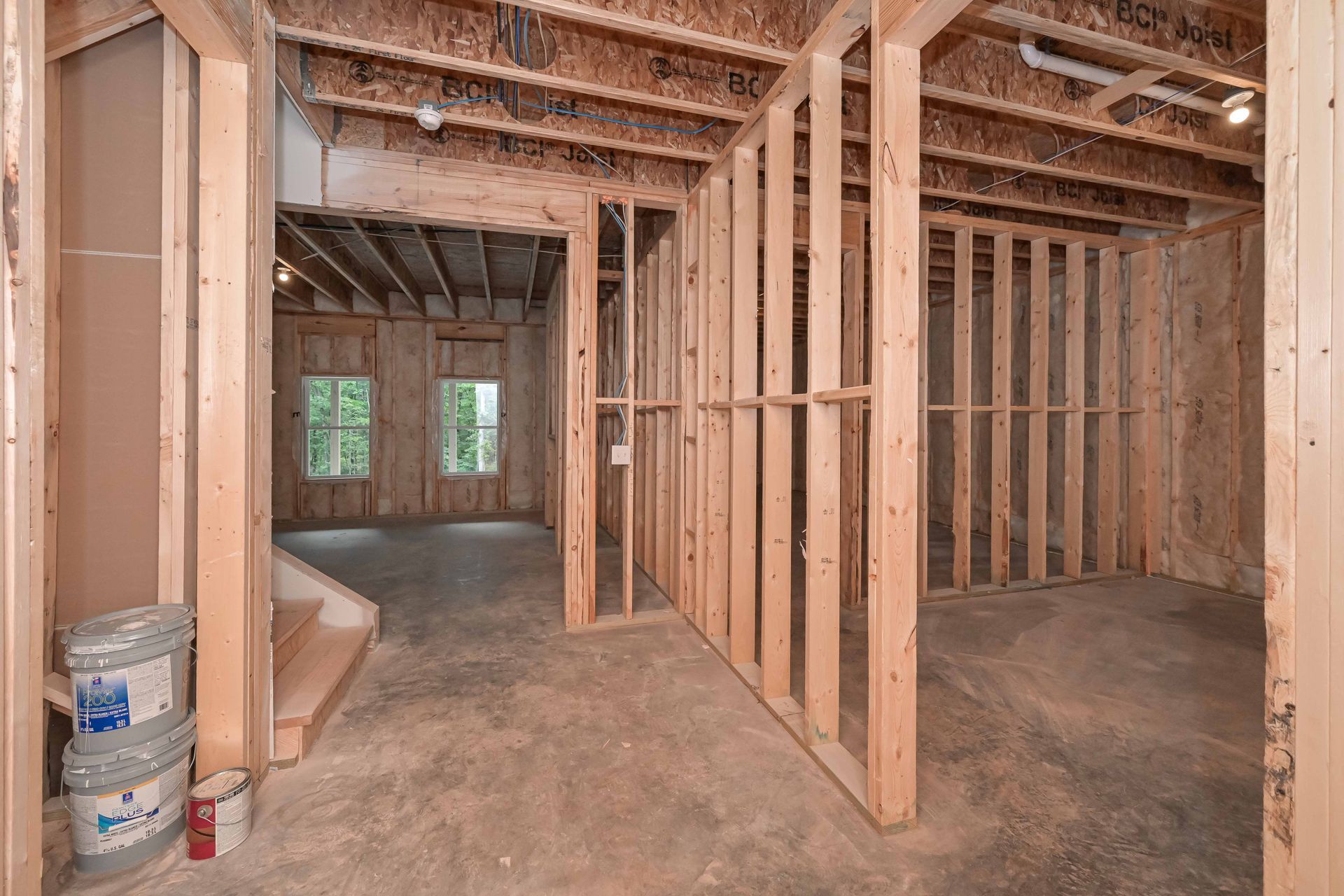 Interior of a room under construction, with wooden framing, exposed beams, and concrete floor.