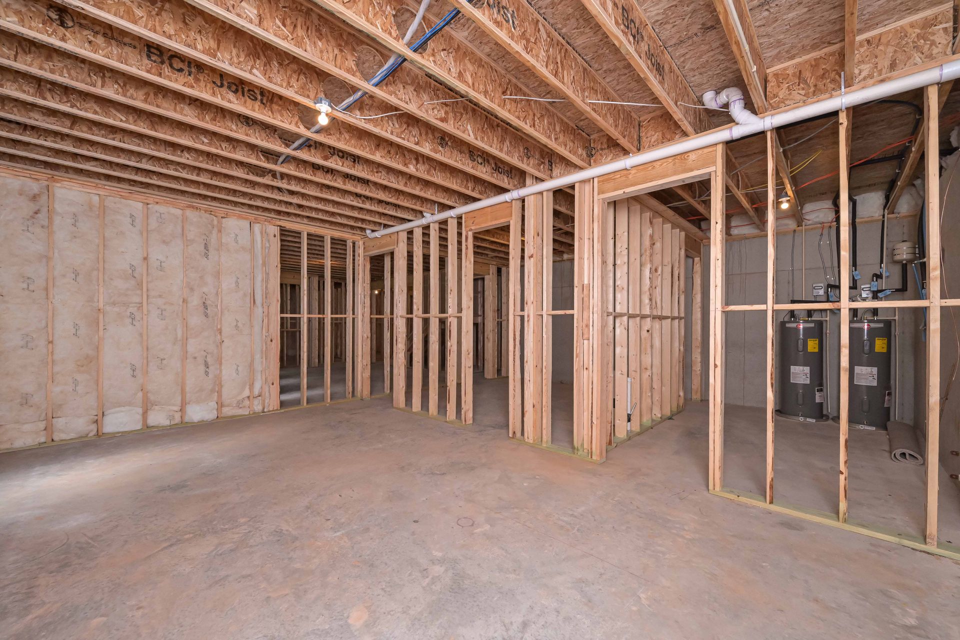 Unfinished basement with exposed wooden studs, concrete floor, and plumbing.