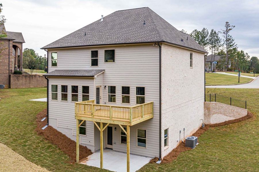Rear view of a two-story home with a wooden deck and a concrete patio in a grassy yard.