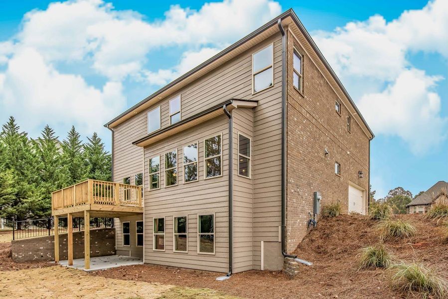Two-story house exterior with a deck, light brown siding, and brick. Overlooking grassy yard and trees against a cloudy sky.