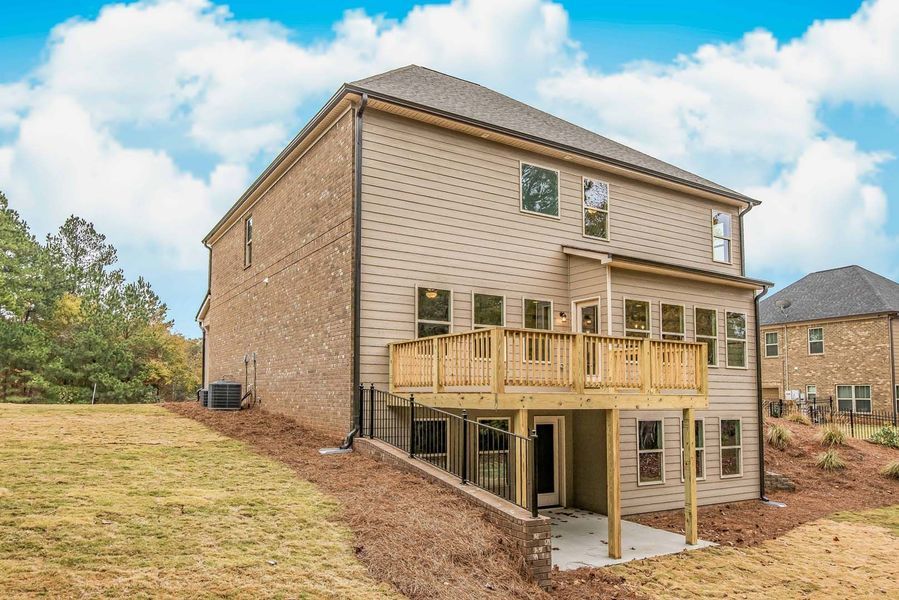 Two-story house with deck, brick, tan siding, and a grassy yard under a partly cloudy sky.