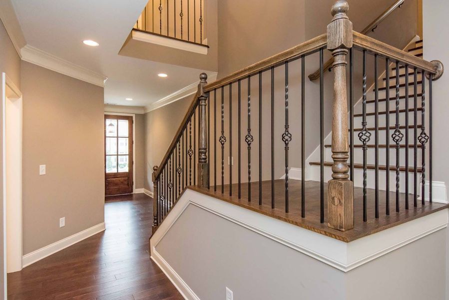 Entryway with wooden staircase, wrought-iron railing, hardwood floors, and a door with glass panes.