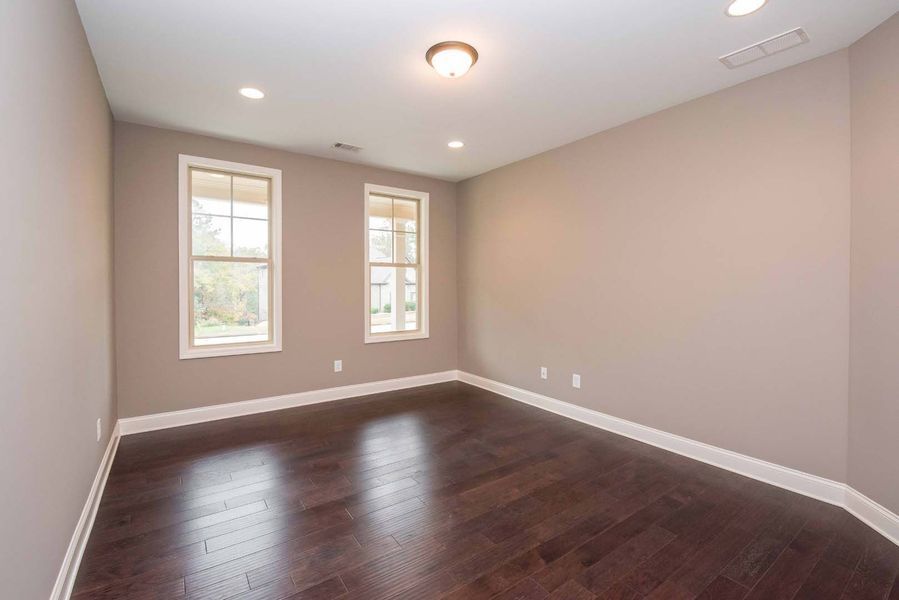 Empty room with two windows and dark wood floors, light brown walls.