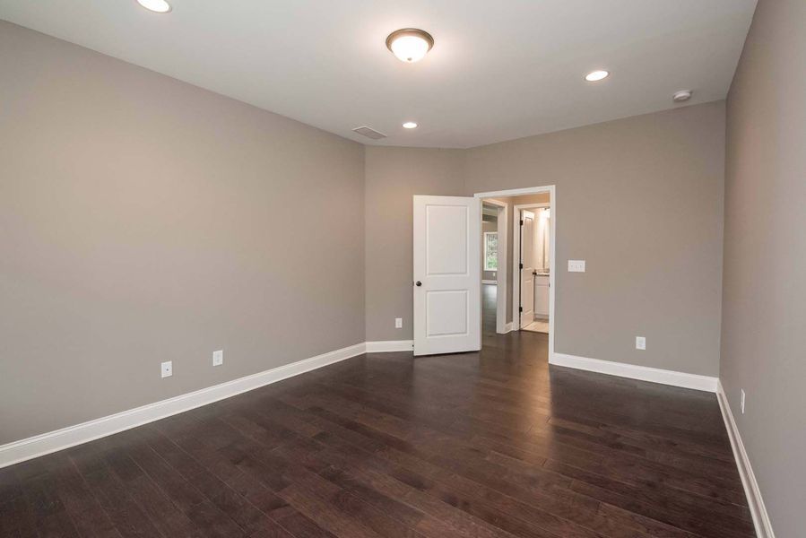 Empty room with dark wood floors, beige walls, and a white door.