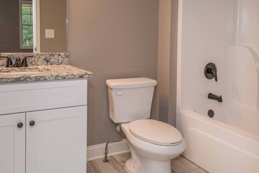 Bathroom with white toilet, vanity, and shower/tub combo; gray walls.