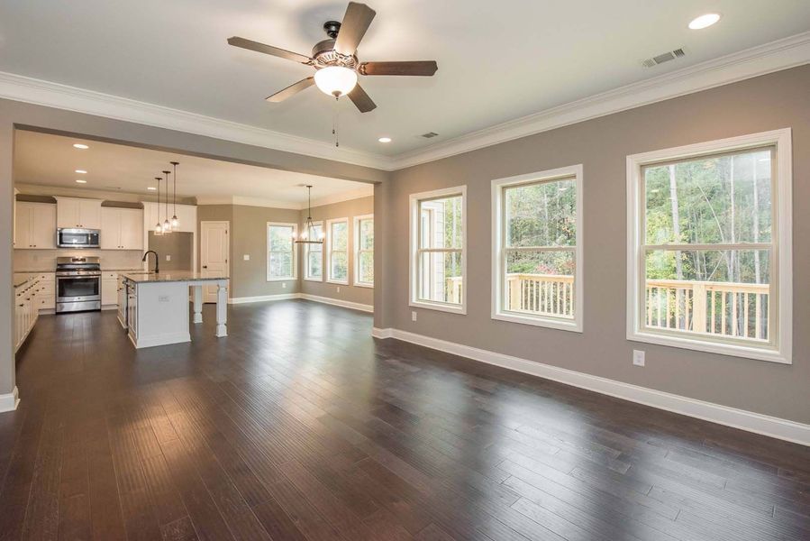 Open-concept living space with hardwood floors, kitchen, and windows overlooking a deck; neutral walls and white trim.