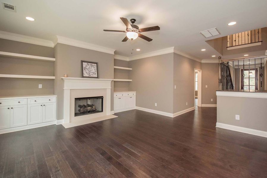 Living room with fireplace, built-in shelves, dark wood floor, neutral walls, and ceiling fan.