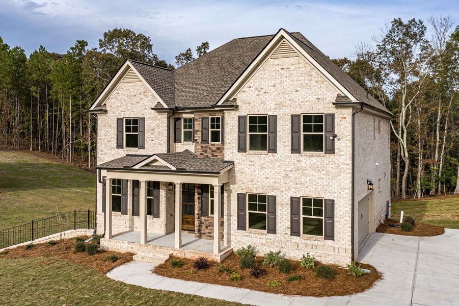 Two-story brick home with a porch and dark shutters, driveway, and surrounding trees.