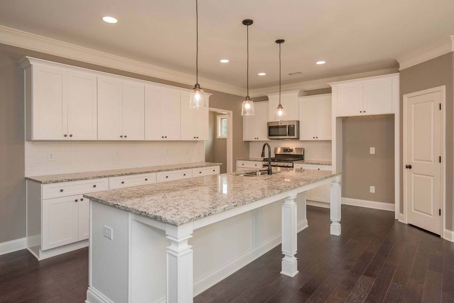 White kitchen with island, granite countertops, pendant lights, dark wood floor, and white cabinets.