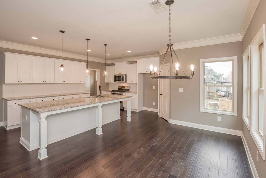 Open kitchen and dining room with white cabinets, island, dark wood floor, and chandelier.