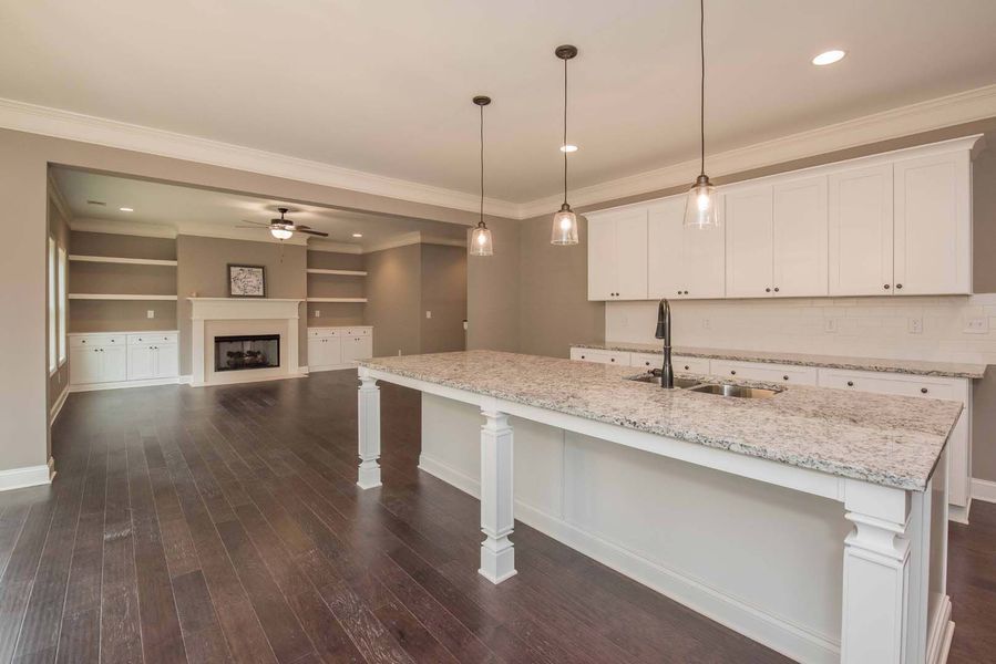 Kitchen with a white island, granite countertop, white cabinets, and dark hardwood floors.