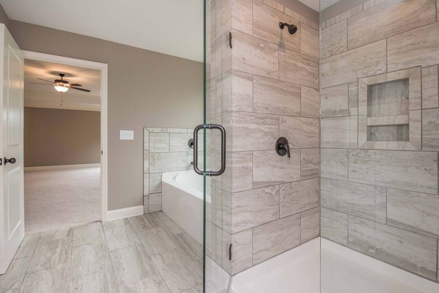 Modern bathroom with glass shower, tub, and doorway to bedroom. Gray tile and neutral colors.