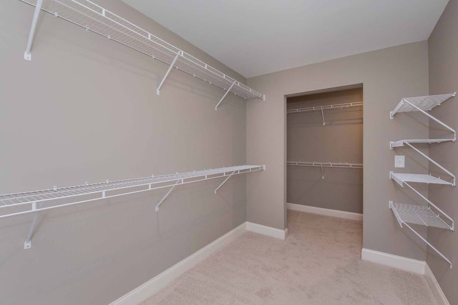 Empty walk-in closet with wire shelves on gray walls and doorway to a second closet.