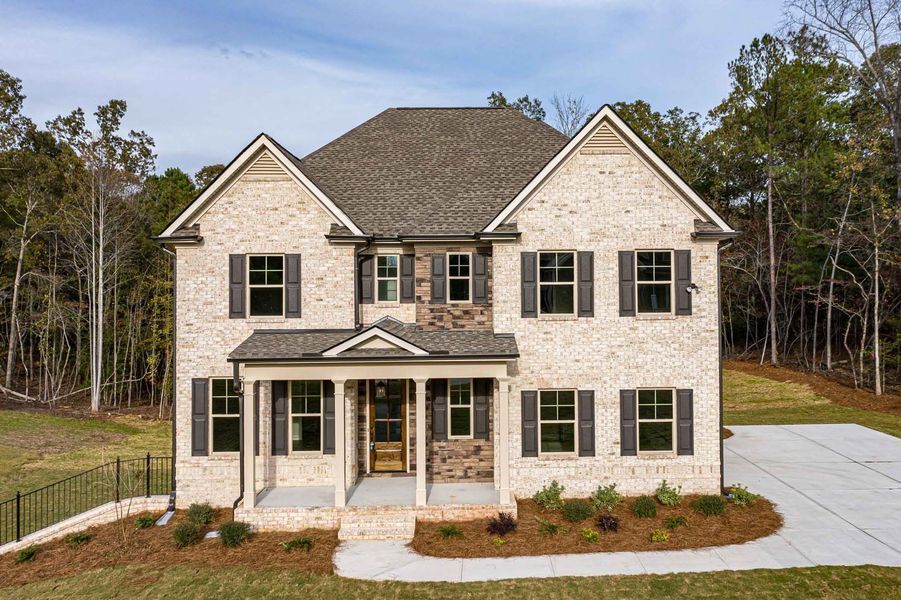 Two-story brick house with dark shutters, front porch, and a gray driveway.