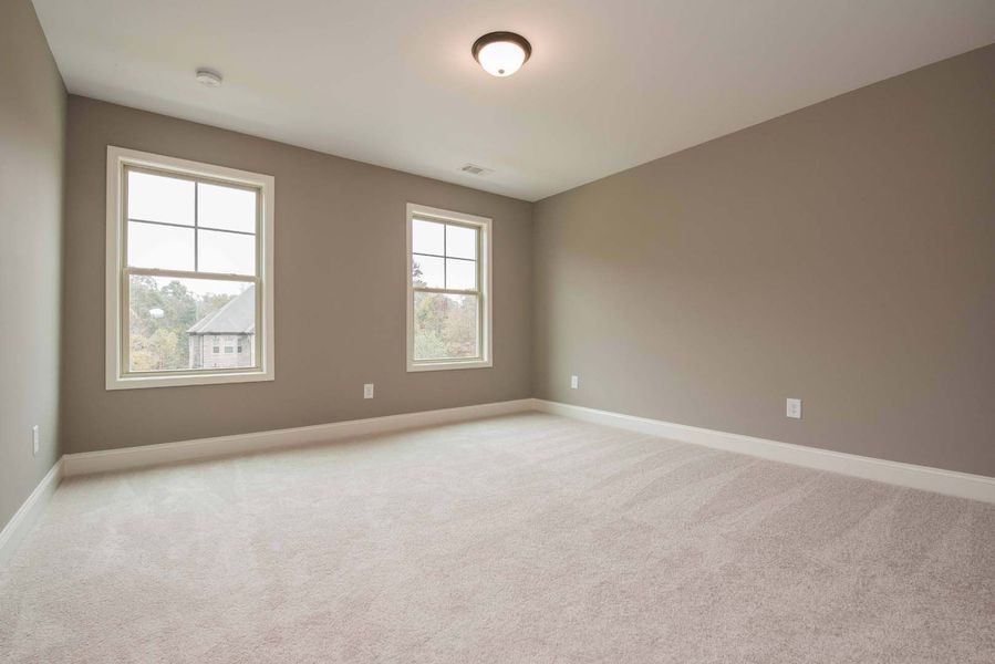 Empty room with beige walls, two windows, and light carpet.