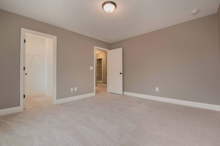 Empty bedroom with neutral walls, carpet, and three doorways.