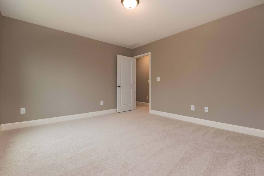 Empty bedroom with beige walls, white trim, carpet, and open doorway.
