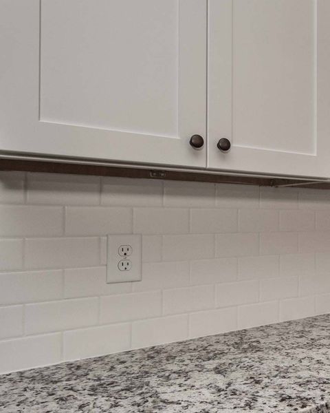 White kitchen cabinets above white subway tile backsplash, outlet visible.