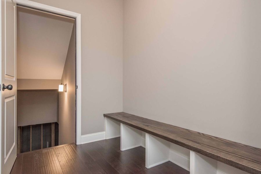 Narrow hallway with wooden bench, a door to the left, and stairs leading down.