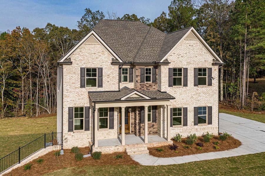 Two-story brick house with black shutters and a gray roof, set on a grassy lot with a driveway.