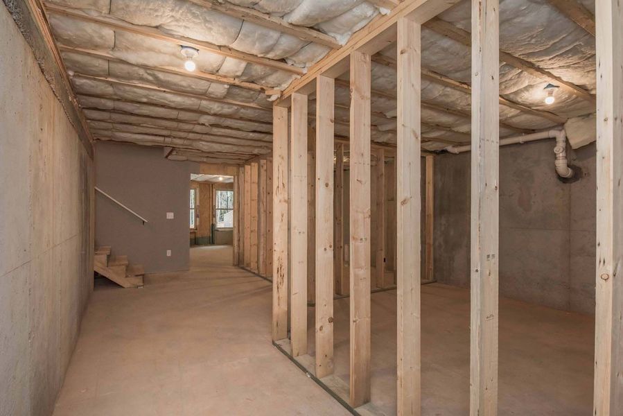 Interior view of an unfinished basement with exposed wooden framing, concrete walls, and stairs.