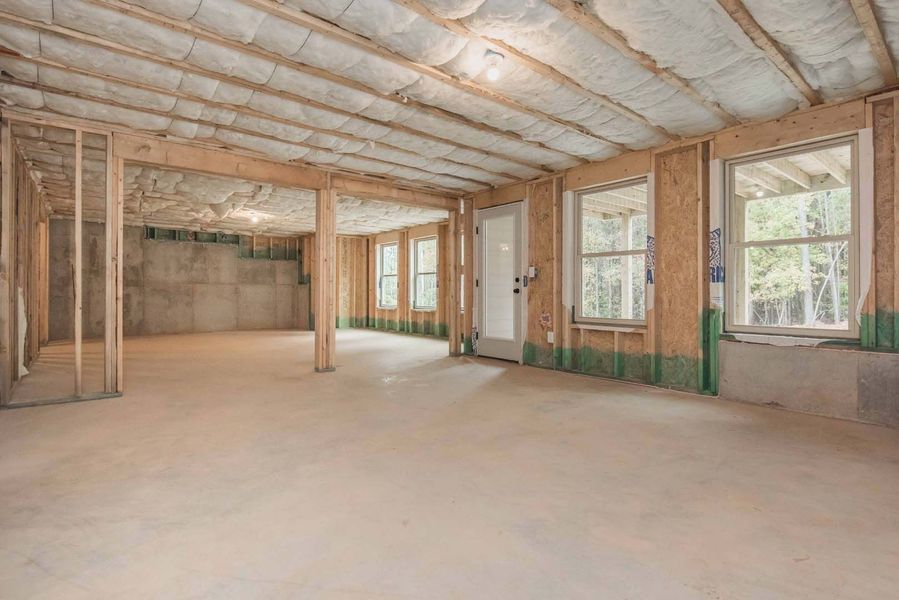 Interior view of an unfinished room with wooden framing, concrete floor, windows, and insulation on the ceiling.