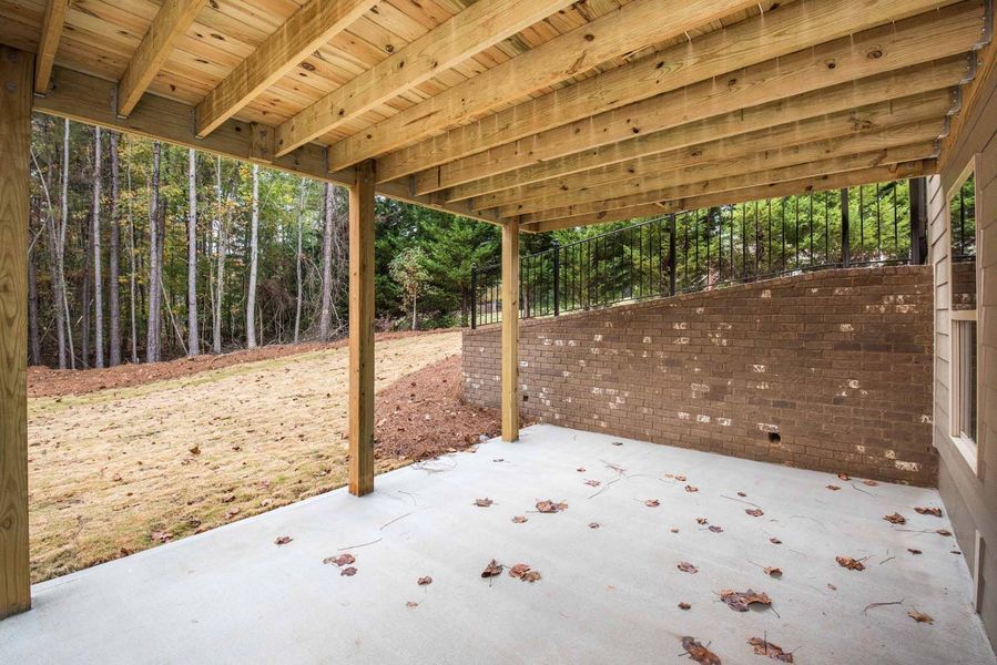 Covered concrete patio with wooden beams and forest backdrop.
